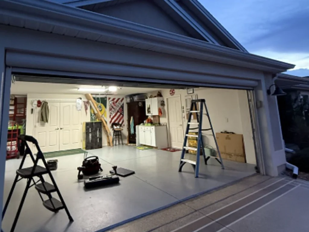 Open garage with tools and storage, ladder leaning, and workout/yard items visible; bright workshop space inside a suburban home garage.